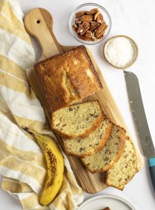 banana bread with coconut and pecans on cutting board with plaid yellow cloth