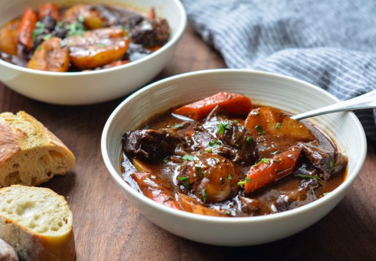 Spoon in a bowl of beef stew with carrots and potatoes.