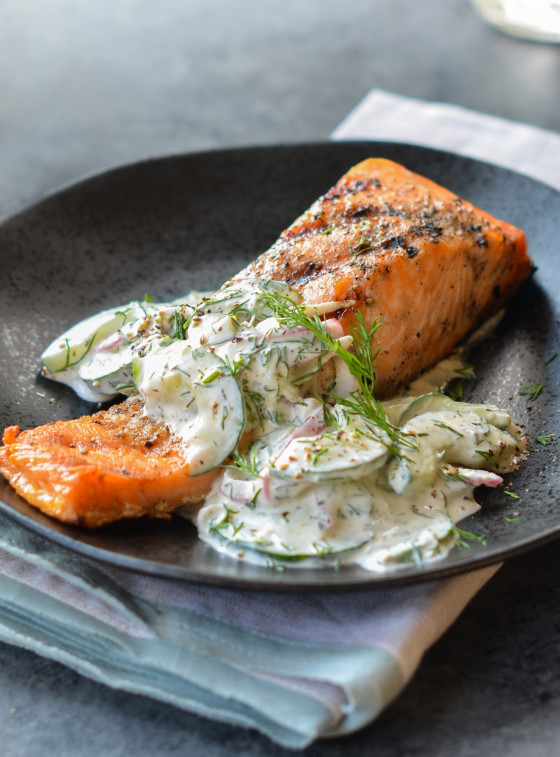 Grilled salmon topped with cucumber-dill salad on a black plate.