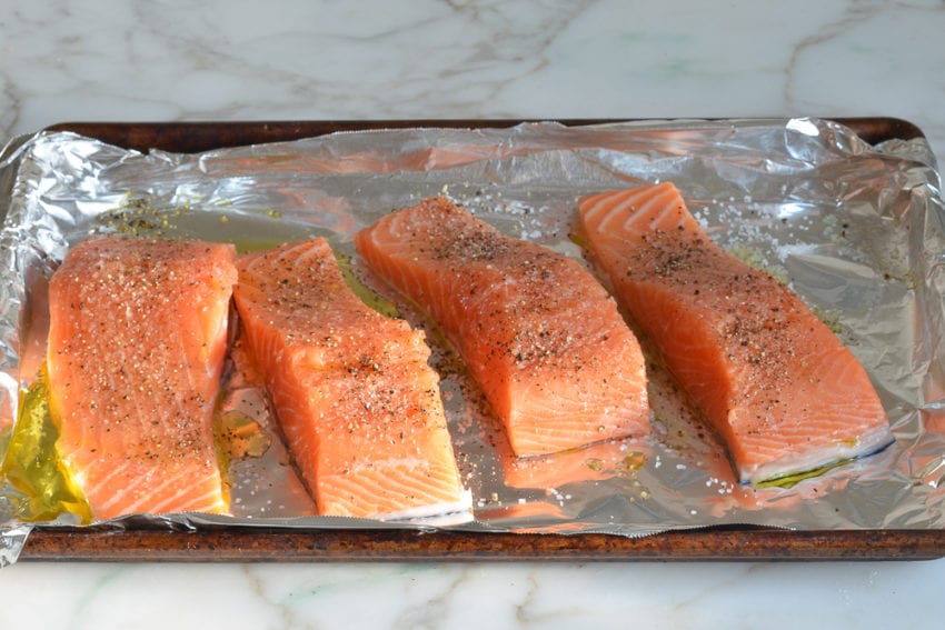 Seasoned salmon filets on a lined baking sheet.