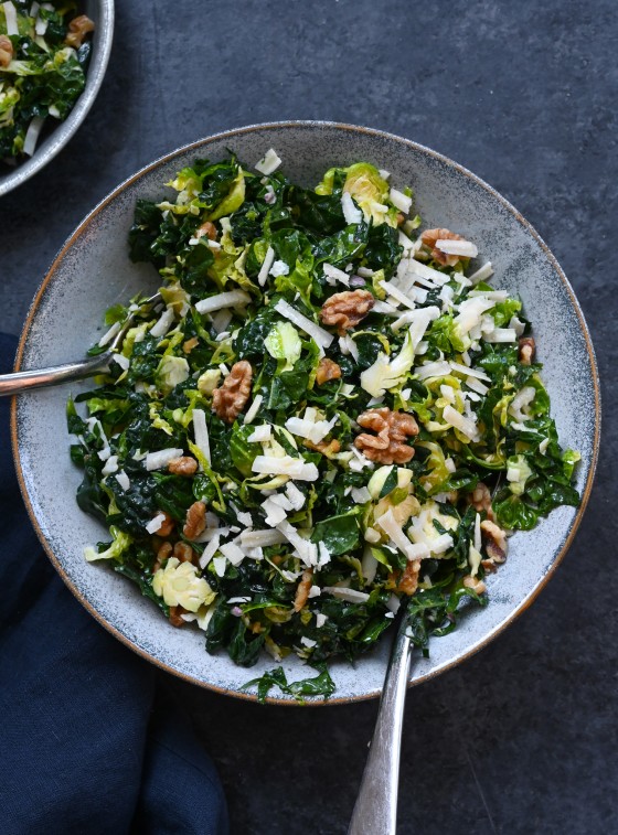 Forks on a plate of kale and brussels sprout salad with walnuts, parmesan, and lemon-mustard dressing.