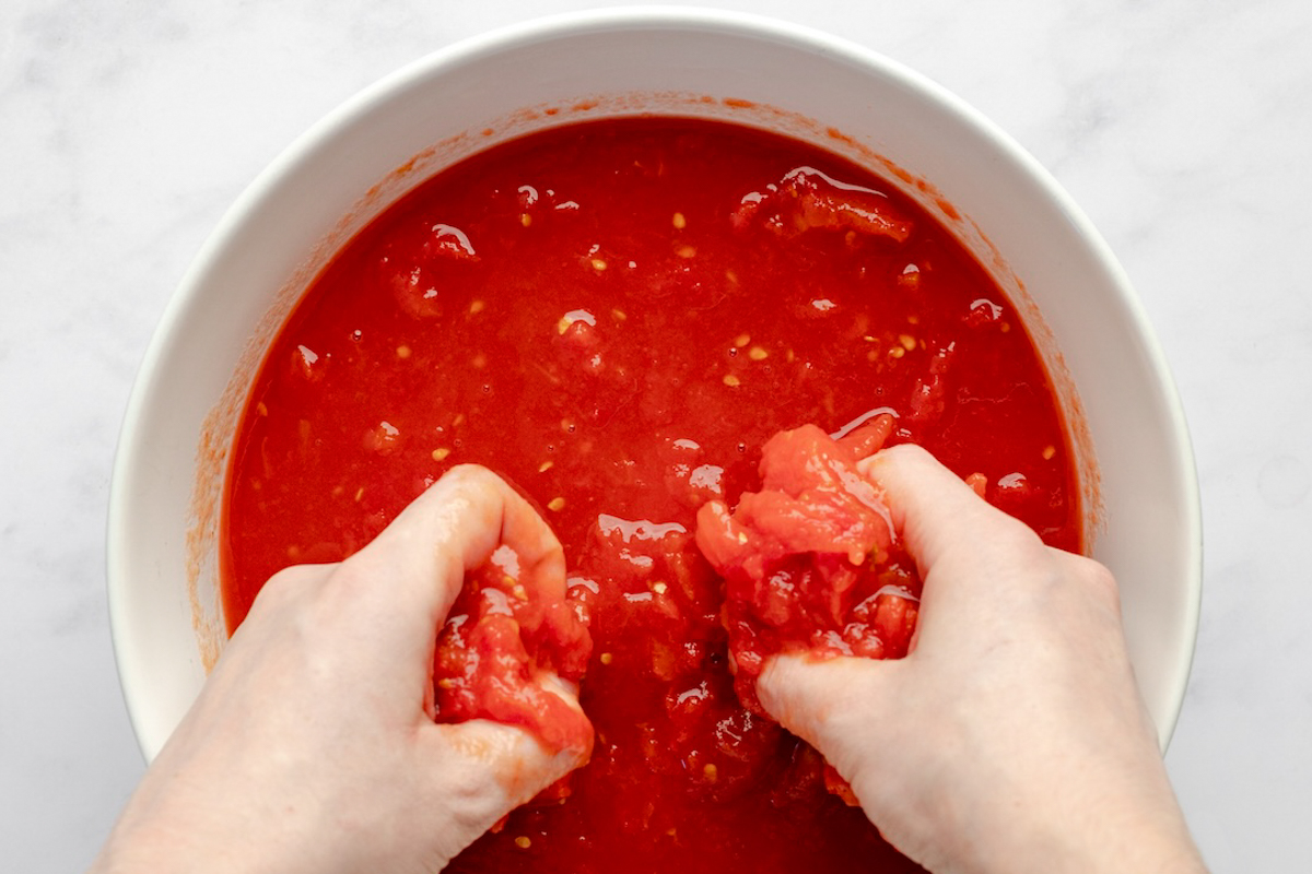 Crushing whole canned tomatoes by hand.