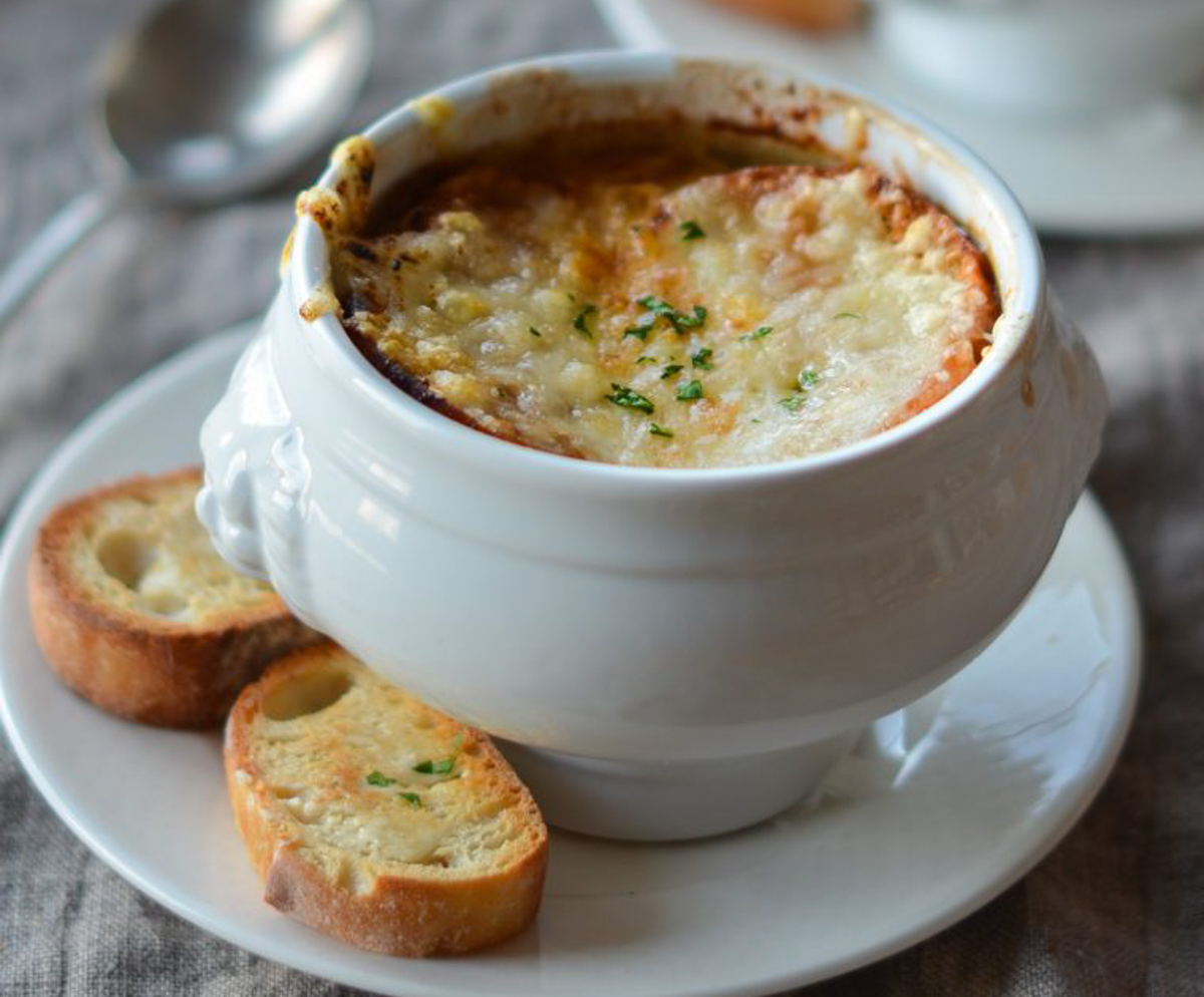 Crock of French onion soup with baguette slices on side.