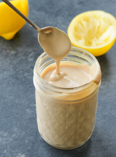 Spoon dripping tahini sauce into a glass jar.