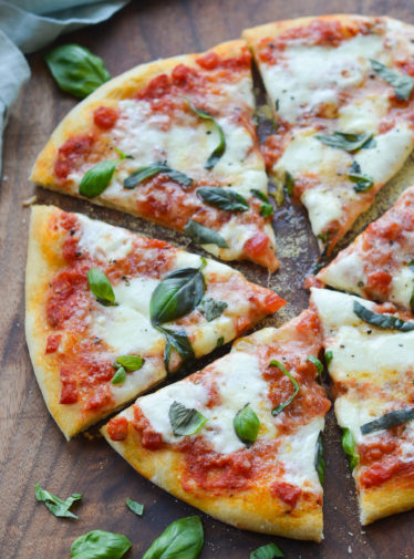 Sliced margherita pizza on a wooden cutting board.