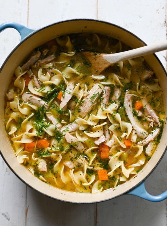 Chicken noodle soup in a Dutch oven with a wooden spoon.