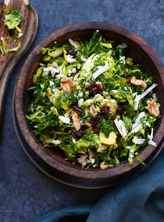 Wooden bowl of kale, brussels sprouts, and dried cranberry salad with honey-dijon vinaigrette.