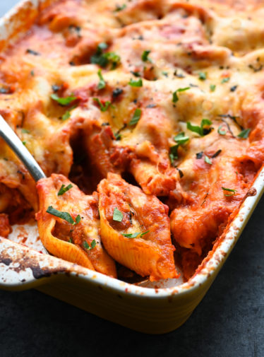 Spoon scooping cheesy stuffed shells from a baking dish.