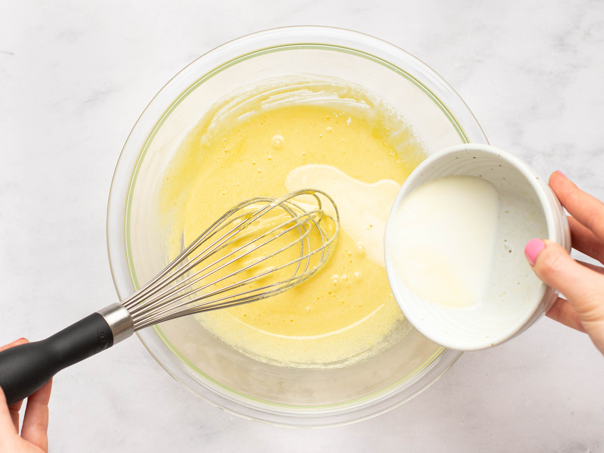 pouring hot milk and butter into the egg and sugar mixture