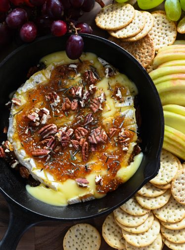 baked brie with crackers, apples, and grapes on wood board