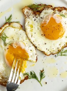 2 crispy fried eggs on white plate with fork poking into runny yolk