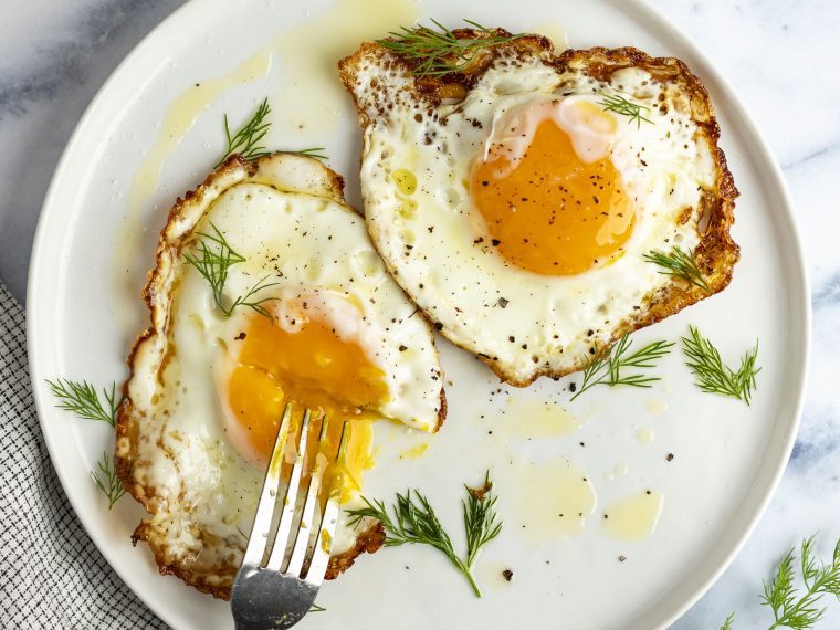 2 crispy fried eggs on white plate with fork poking into runny yolk