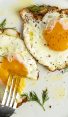 2 crispy fried eggs on white plate with fork poking into runny yolk