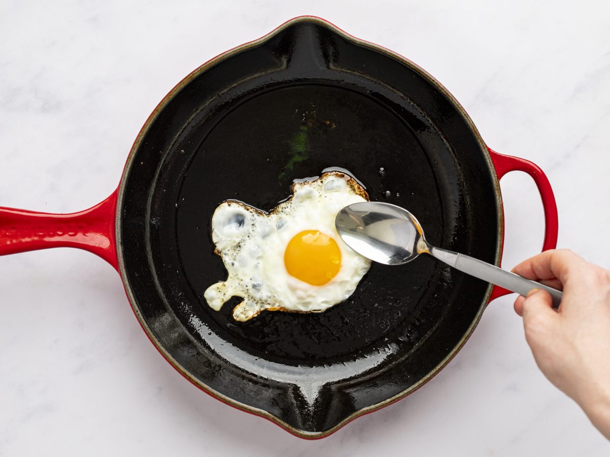 spooning oil over the egg while cooking in cast iron skillet