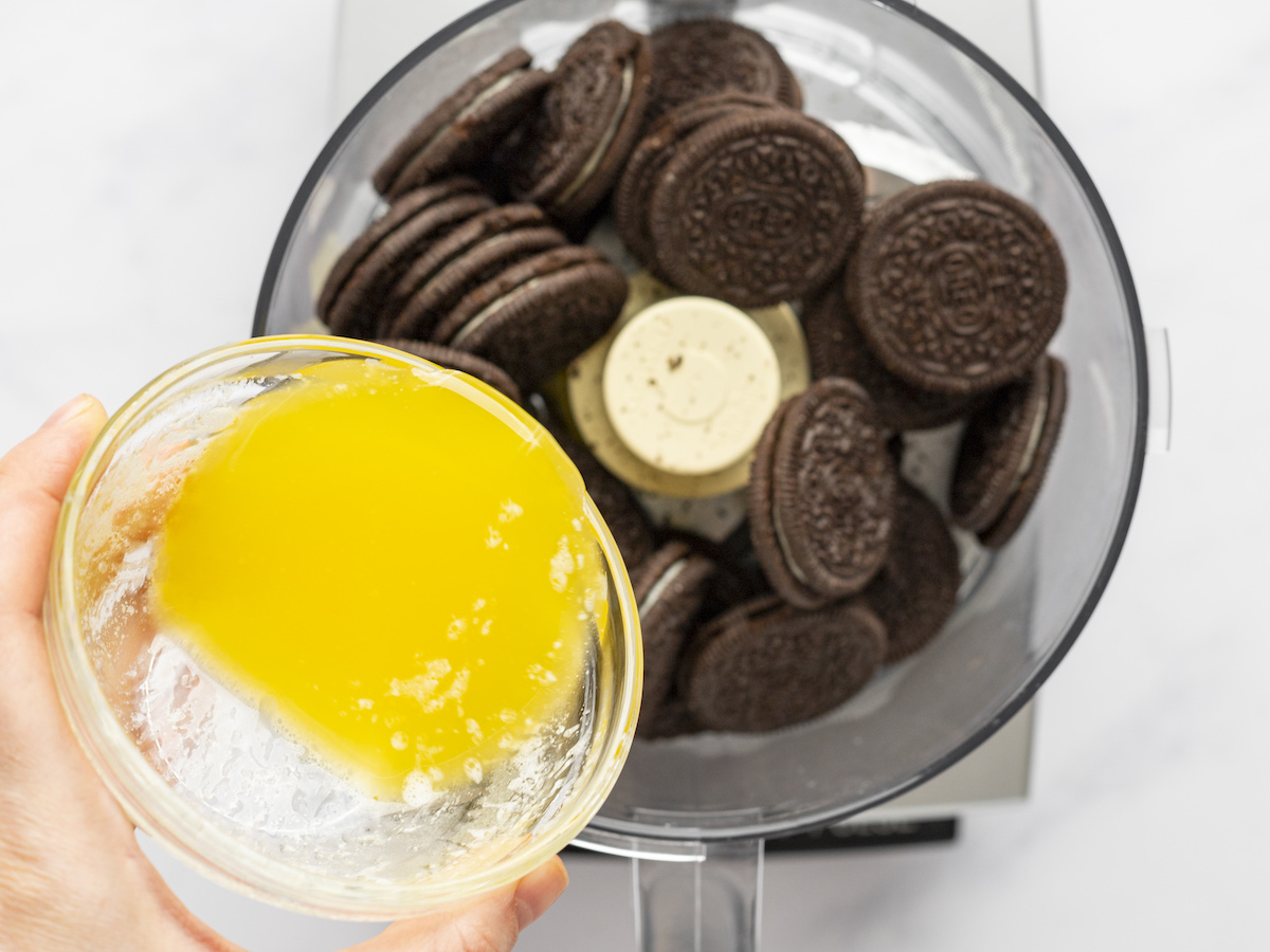 pouring melted butter into food processor filled with oreos.