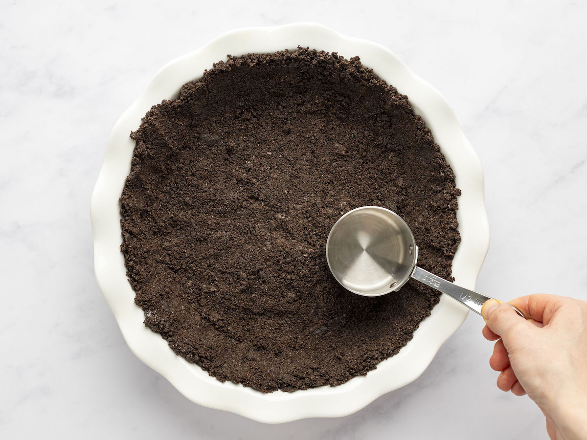 pressing the cookie crumbs into the pie dish with a measuring cup.