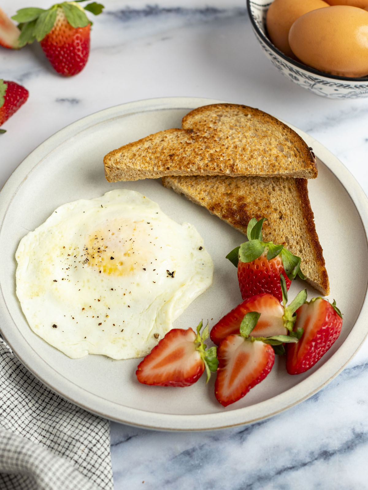 over easy egg on white plate with strawberries and 2 triangles of toast