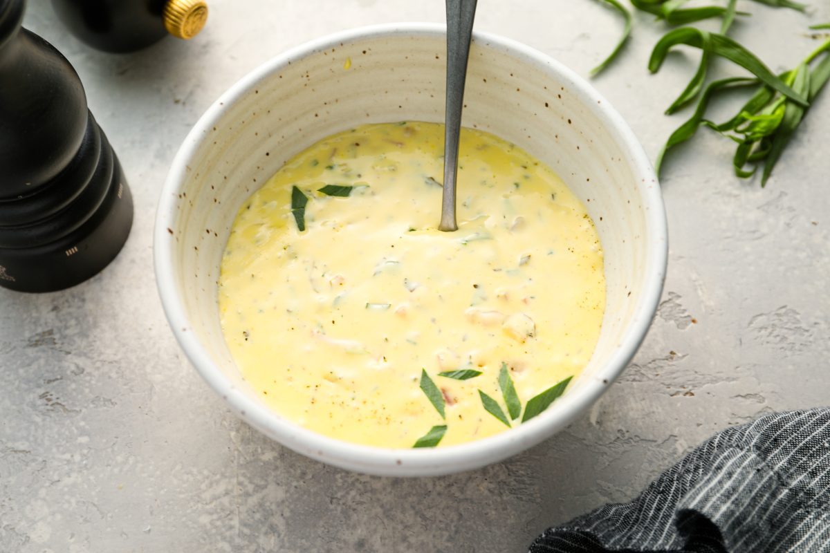 bearnaise sauce in white bowl with pepper grinder, fresh tarragon, and napkin nearby