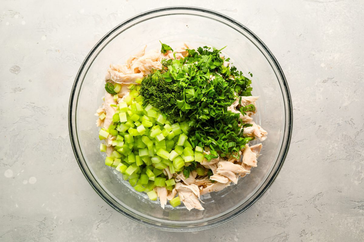 adding chicken, celery, herbs, and scallions to dressing for chicken salad.