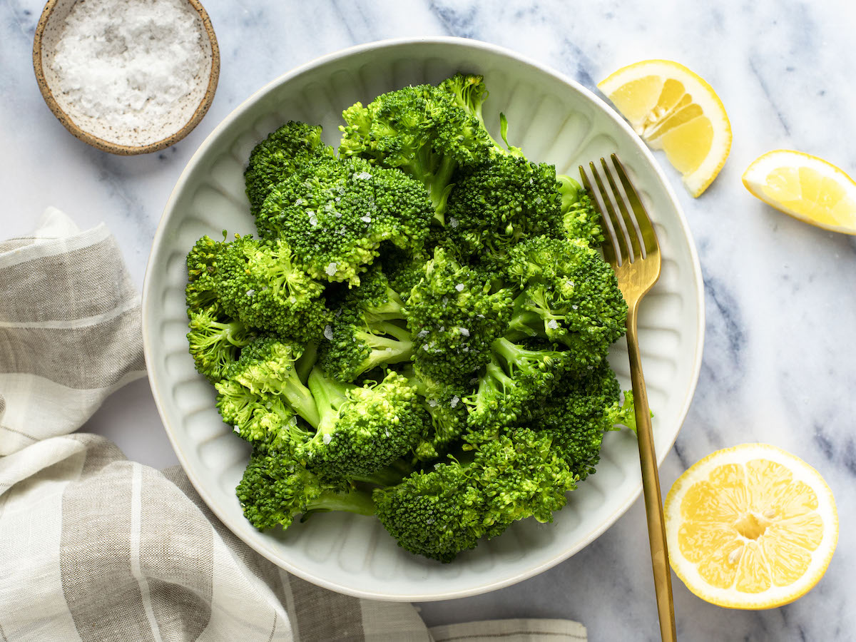 steamed broccoli in bowl with lemon wedges and salt