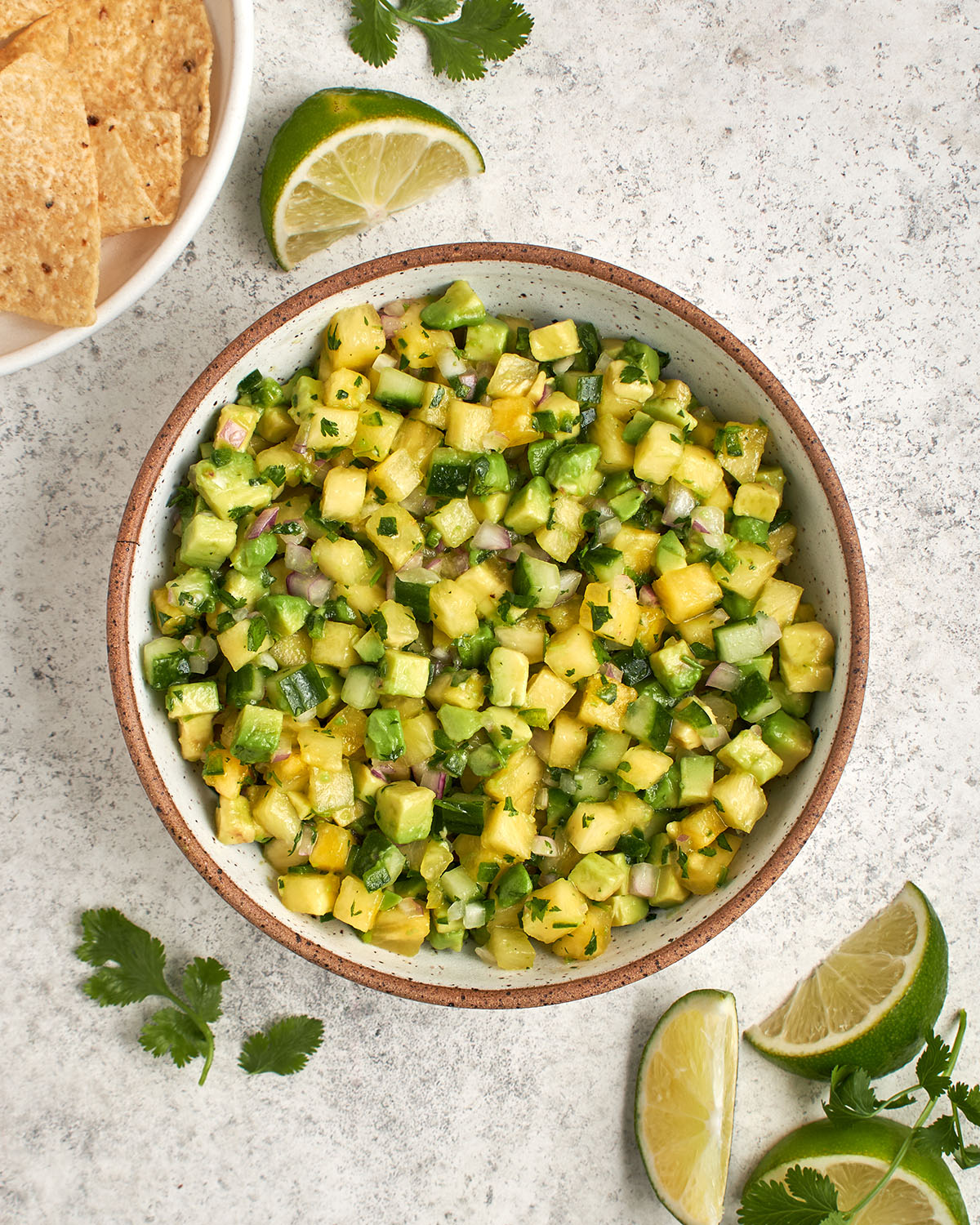 pineapple avocado salsa in bowl surrounded with lime wedges and a white bowl with tortilla chips