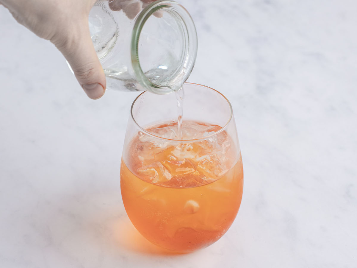 soda water added to large wine glass with ice cubes, Prosecco, and aperol 