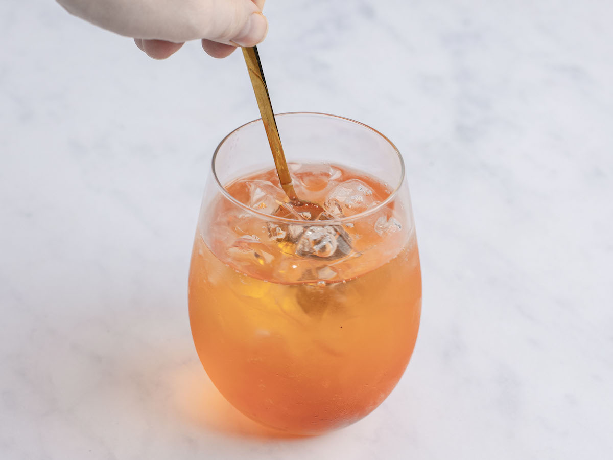 stirring Prosecco, aperol, and soda water in large wine glass with ice cubes 