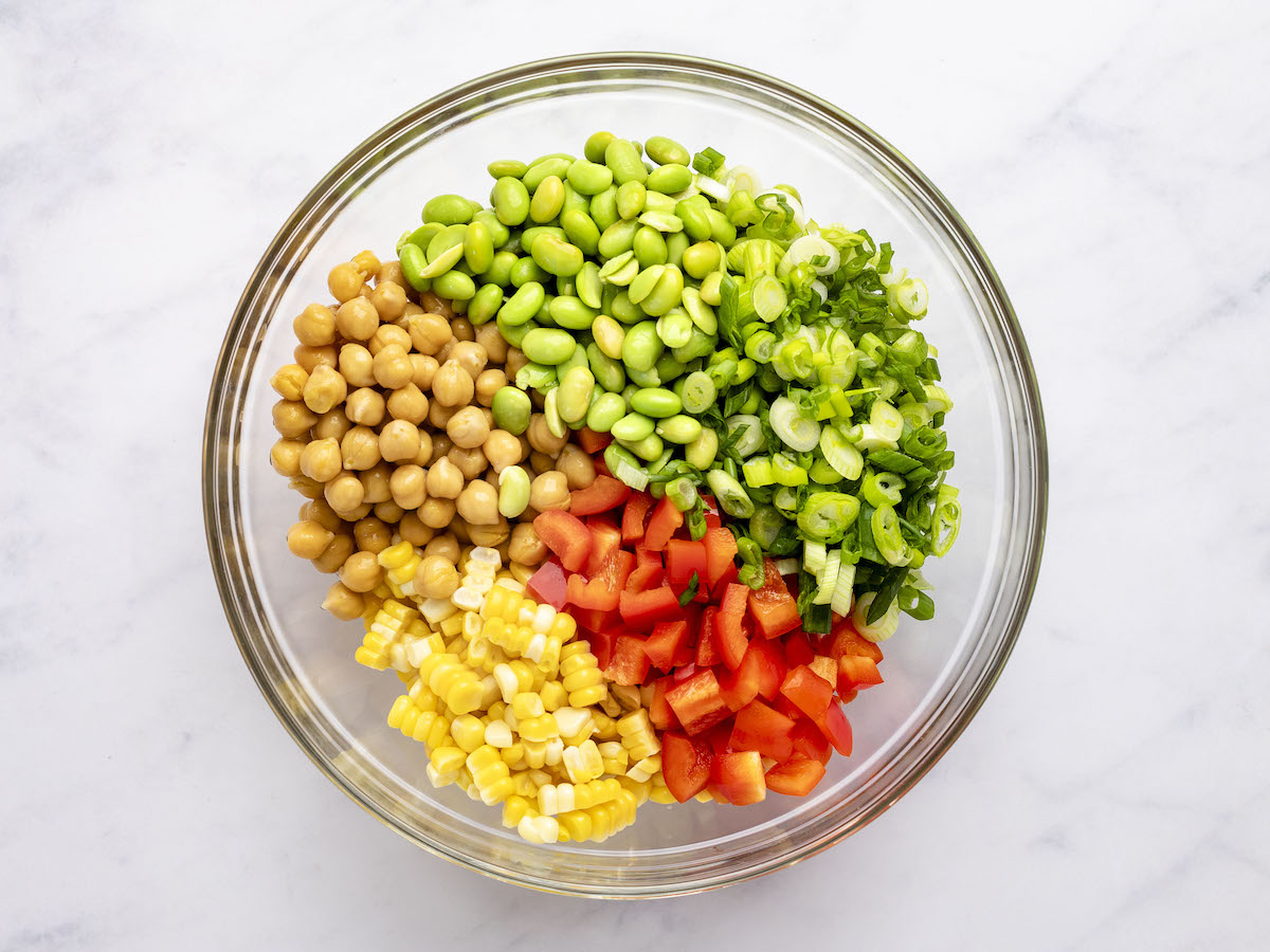 chickpeas, red pepper, corn kernels, edamame, and scallions in separate piles in large glass bowl