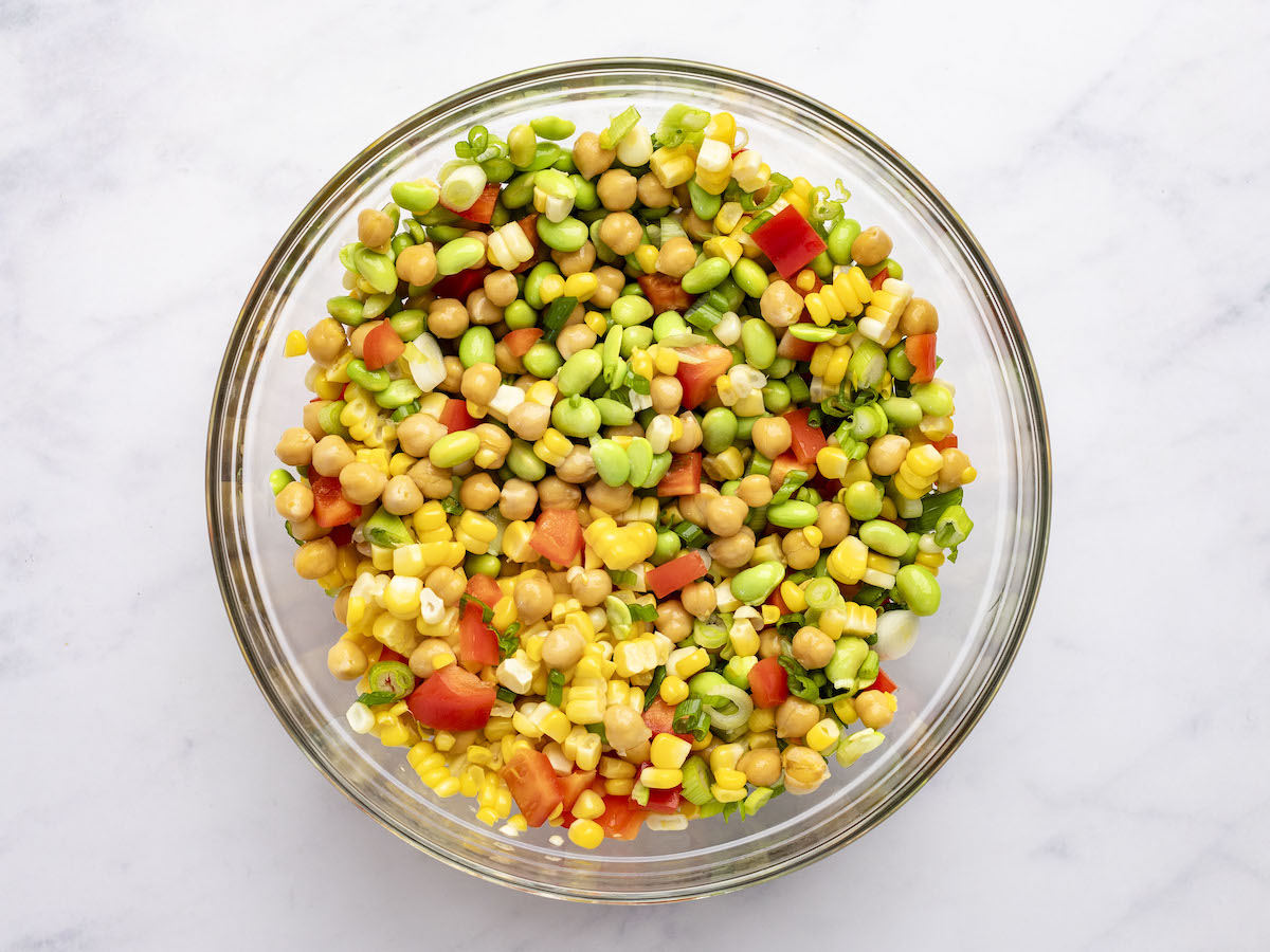 chickpeas, red pepper, corn kernels, edamame, and scallions combined in large glass bowl