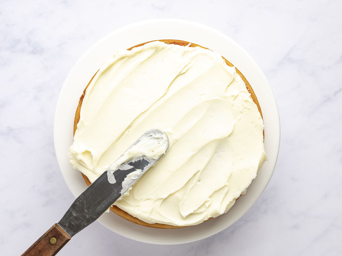 offset spatula spreading frosting on bottom cake layer