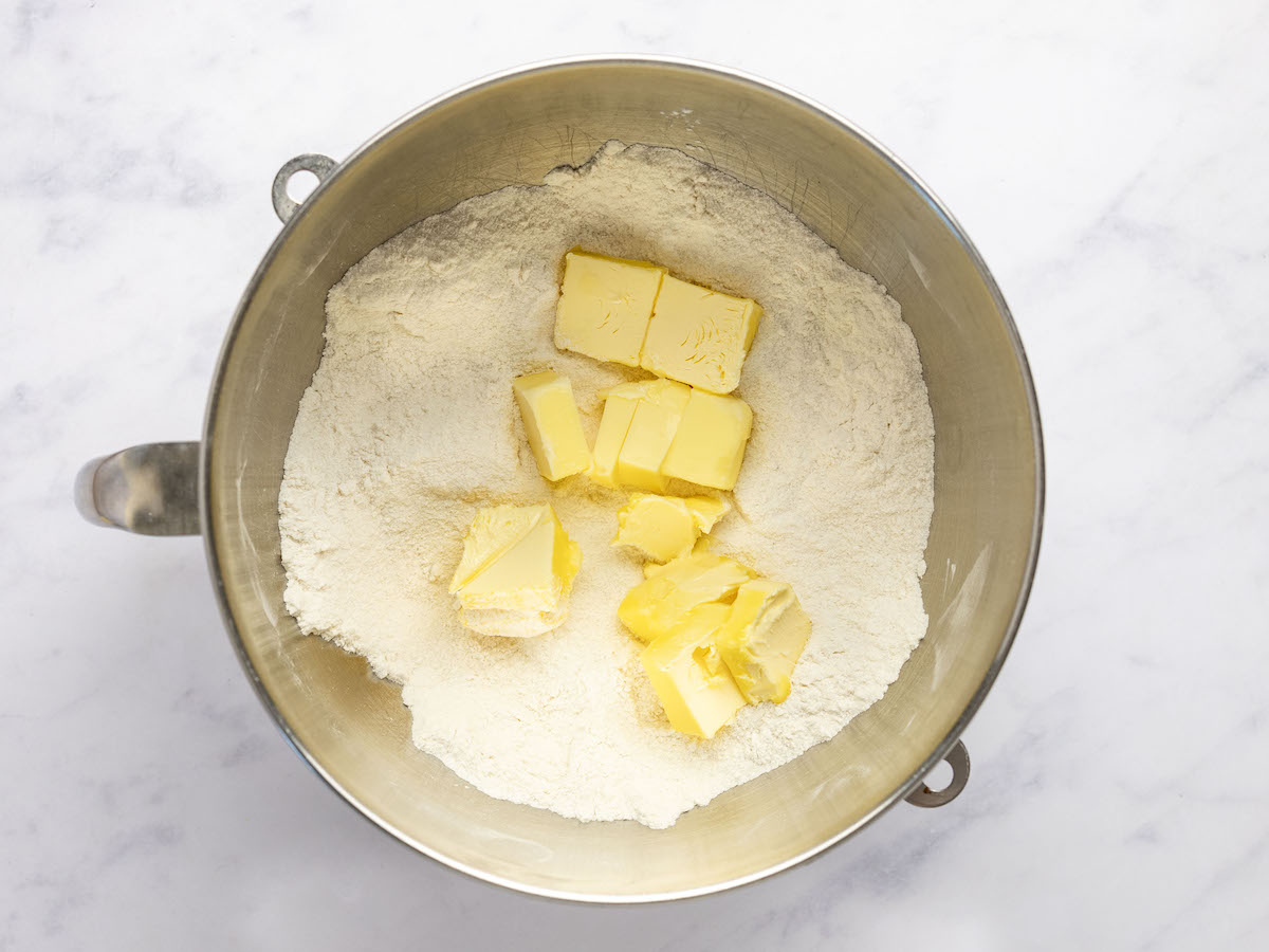 butter added to mixing bowl with mixture of flour, sugar, baking powder, and salt