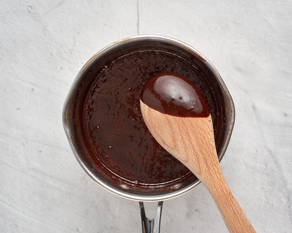 glossy, thick hot fudge in saucepan with wooden spoon