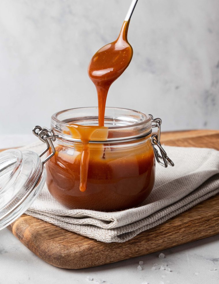 Jar of homemade caramel sauce on wooden board