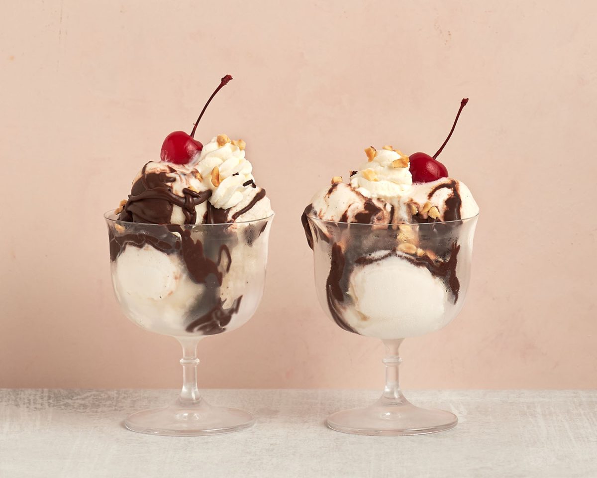 2 hot fudge sundaes in sundae glasses sitting next to each other