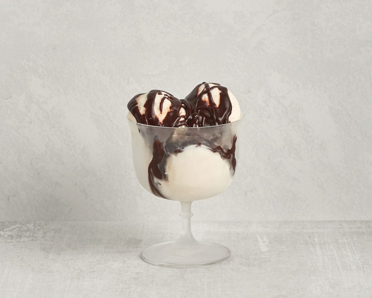 sundae glass with 3 scoops of vanilla ice cream with hot fudge on top