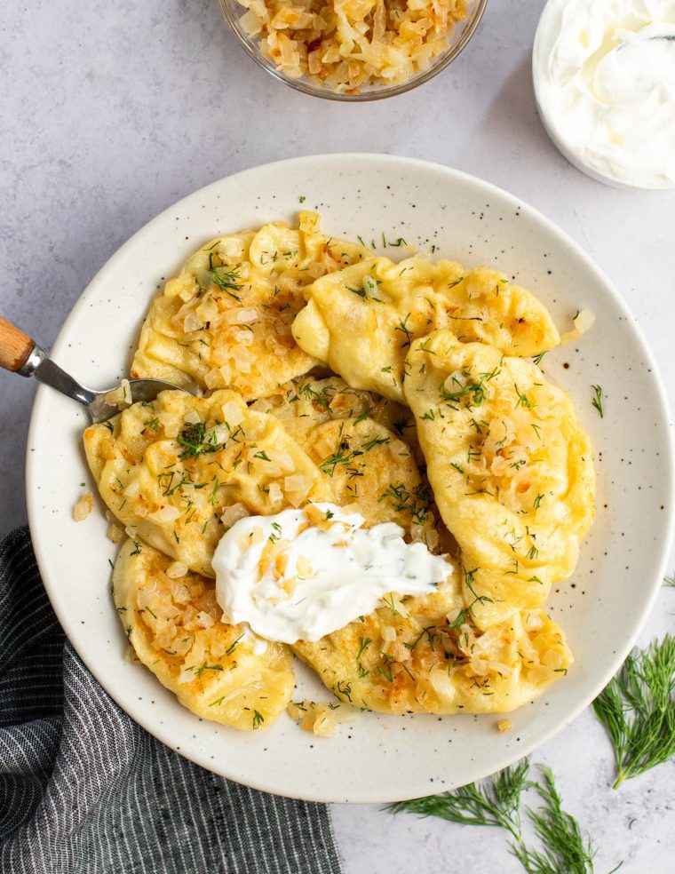 pierogi on plate with sour cream and onions