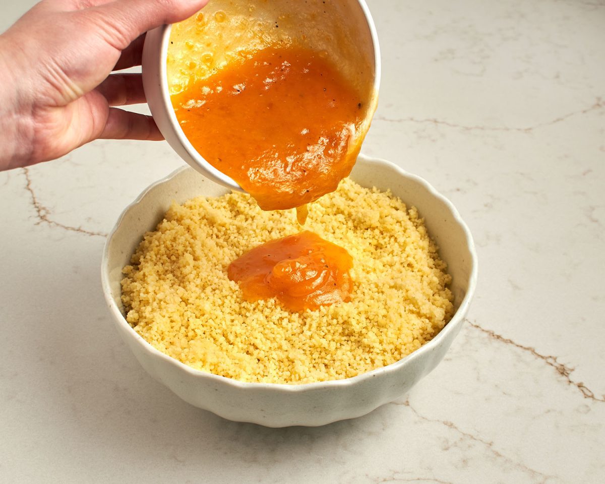 pouring apricot vinaigrette into white serving bowl with cooked couscous