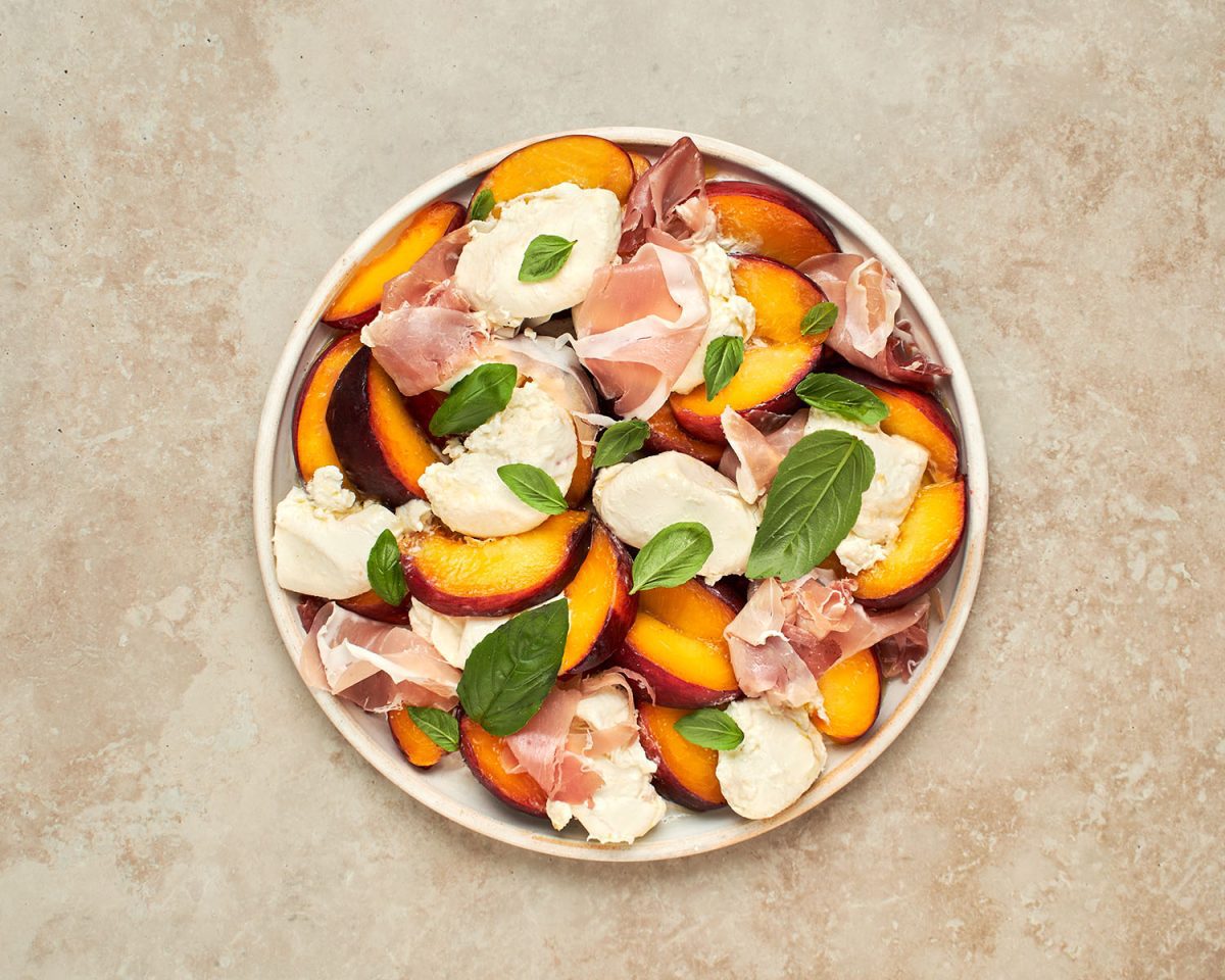 peaches, prosciutto, burrata and basil on white round platter