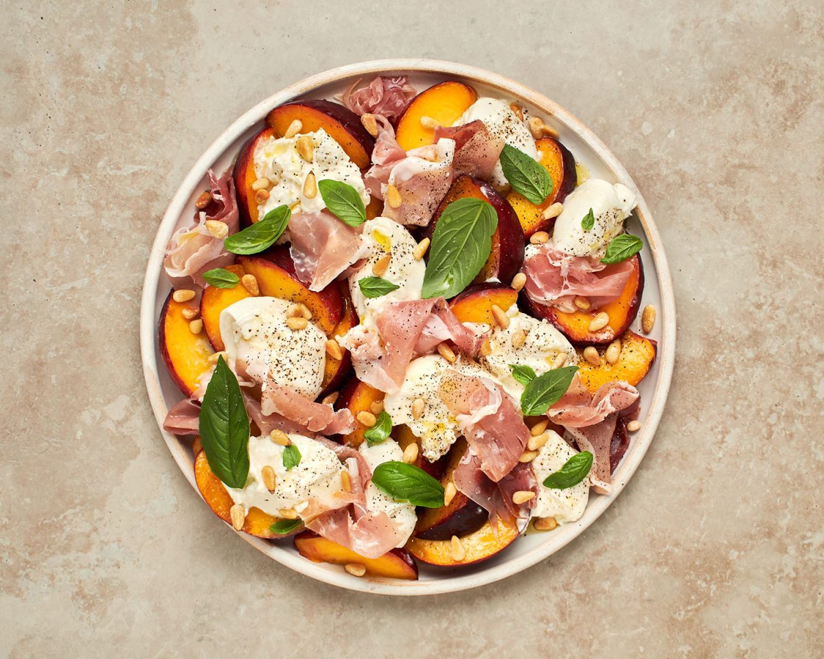 finished peach burrata and prosciutto salad with salt, pepper, oil, vinegar, and pine nuts on top