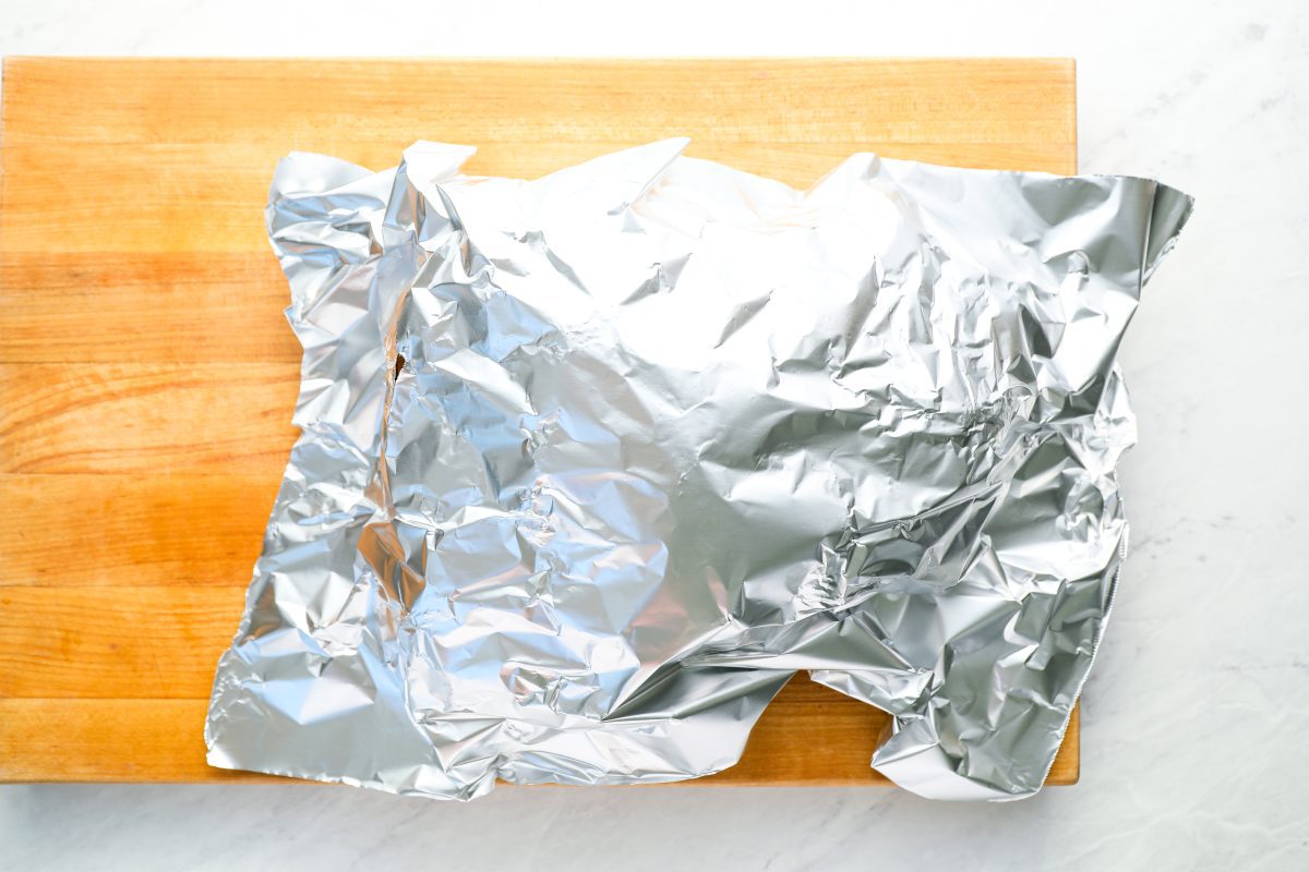 pork butt covered with foil resting on cutting board