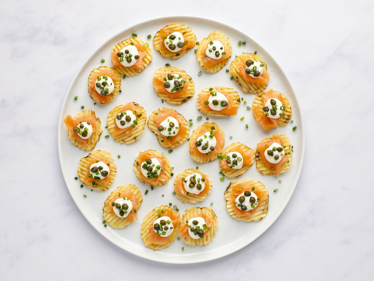 potato chips on white serving plate topped with smoked salmon, cream cheese mixture, capers and chives