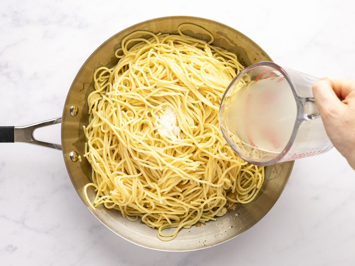 pouring 3/4 cup pasta cooking liquid into skillet with spaghetti