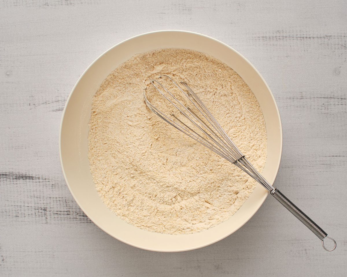 flour, cornmeal, sugar, baking powder, and salt combined in white bowl with whisk