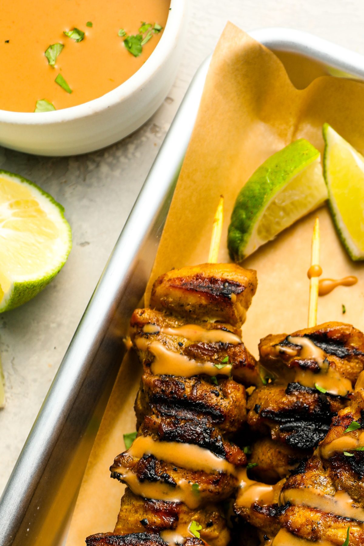 small white bowl with thai curry peanut sauce next to baking sheet with chicken skewers drizzled with the sauce 