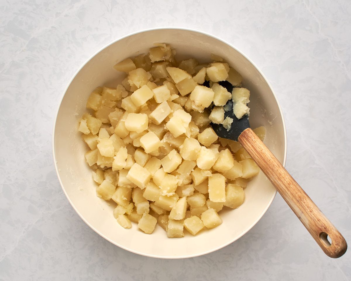 cooked potatoes tossed with vinegar in large white bowl