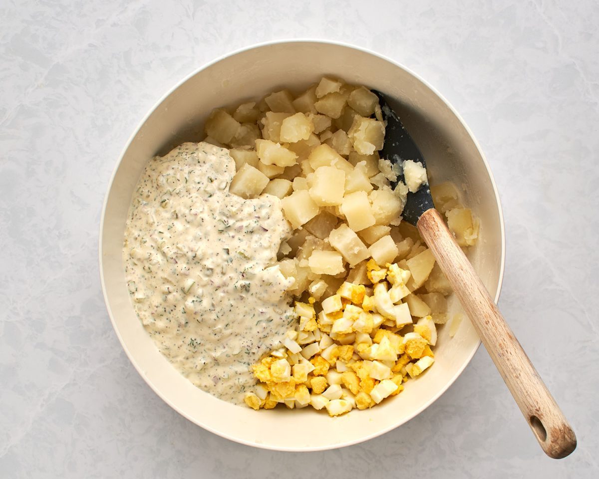 dressing added to potatoes and diced eggs in large white bowl