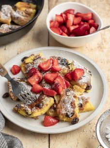 confectioner sugar dusted kaiserschmarrn on white plate with strawerry pieces scattered on top