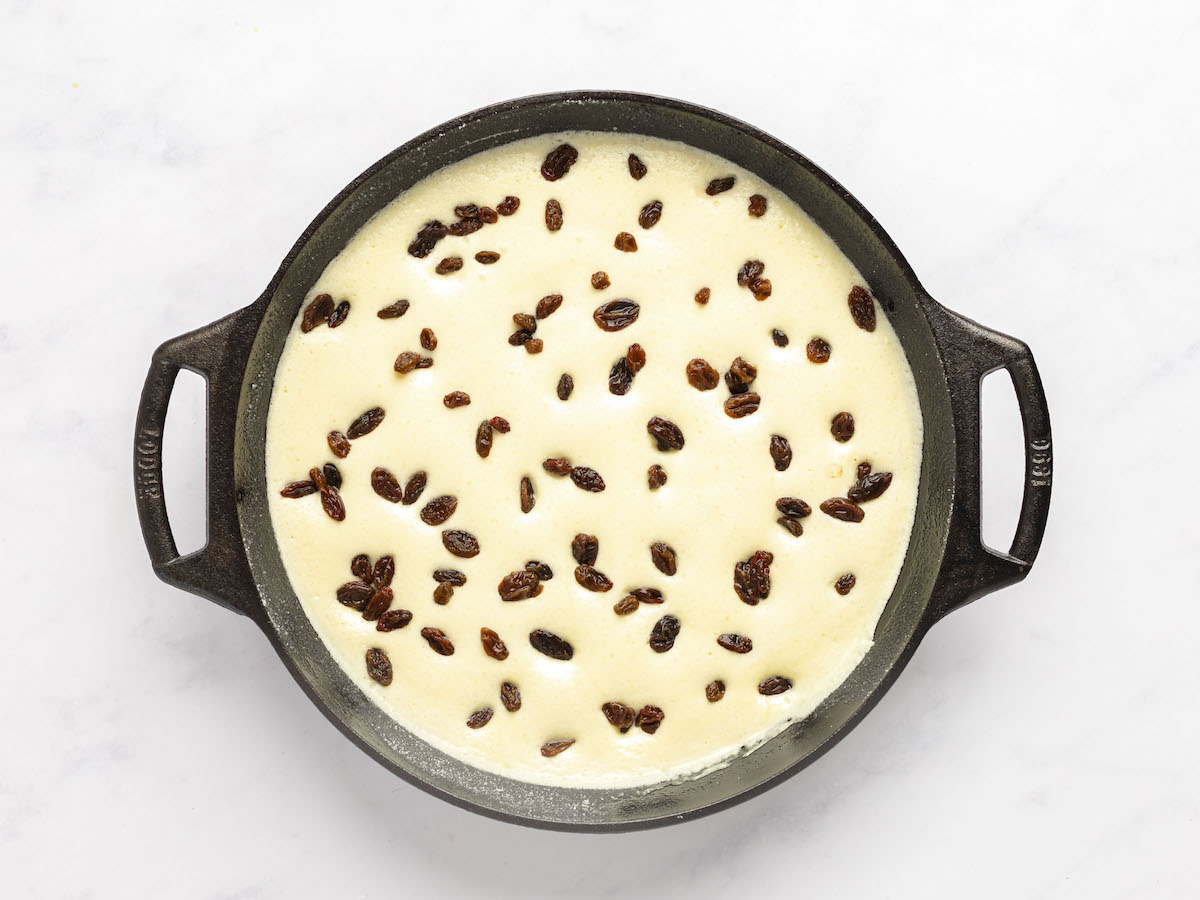 10-inch skillet with rum-steeped raisins evenly distributed in partially cooked batter