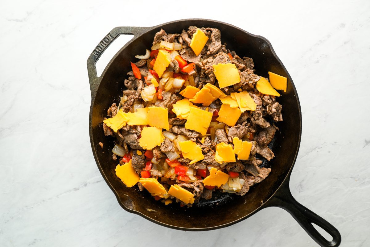 cooked meat and vegetables and american cheese pieces in large cast iron skillet