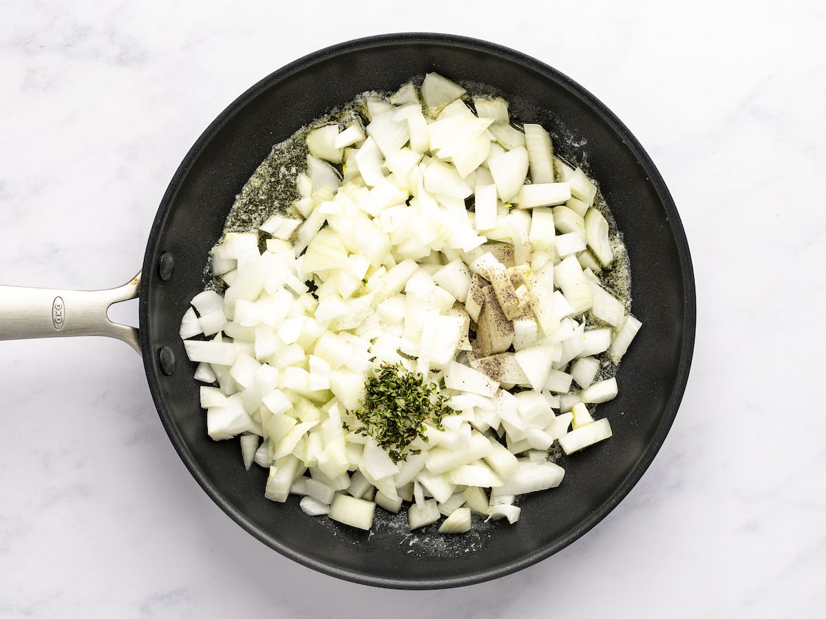 large skillet with onions, salt, pepper, and thyme added to butter